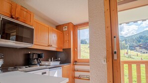 A kitchen with wooden cabinets, a built-in stove, and a window overlooking a mountainous landscape. - Valmorel: 32m² apt, ski-in/ski-out, balcony, ski locker (Valmorel)