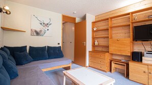A modern living room with a sofa, a small table, wooden shelving, and a television. - Valmorel: 32m² apt, ski-in/ski-out, balcony, ski locker (Valmorel)