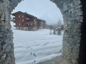 Paisaje nevado con un arco de piedra enmarcando un edificio de varios pisos y balcones.