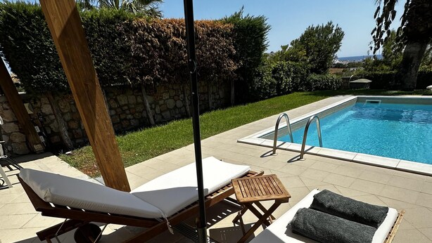 A poolside area with lounge chairs, a small table, and a stone wall in the background. - Charaki Coastal Villa Retreat (Rhodes)