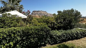 A view of a rocky hill with a white structure on top, surrounded by dense green foliage and a clear blue sky. - Charaki Coastal Villa Retreat (Rhodes)