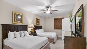 Habitación de hotel con dos camas, ventilador de techo, escritorio con espejo y televisor.
