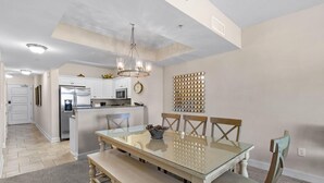 Una cocina moderna con armarios blancos, un refrigerador de acero inoxidable y un comedor con una mesa de vidrio y sillas de madera.