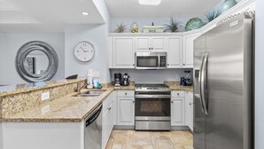 A modern kitchen with white cabinets, stainless steel appliances, granite countertops, and a tiled floor.