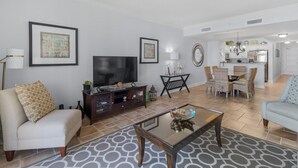 A living room with a sofa, coffee table, TV, and a dining area with chairs.