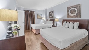A hotel room with two beds, a wooden headboard, a nightstand with a lamp, a mirror, and a vase with flowers.