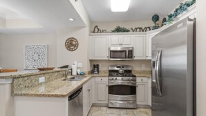 A modern kitchen with white cabinets, stainless steel appliances, and a granite countertop. - Sandy Toes Paradise Retreat: 2BR Oceanfront Condo (North Myrtle Beach)