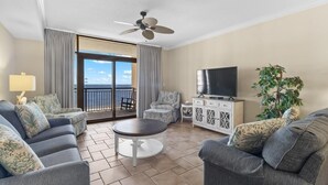 A spacious living room with a balcony, a ceiling fan, a flat-screen TV, and a potted plant. - Sandy Toes Paradise Retreat: 2BR Oceanfront Condo (North Myrtle Beach)