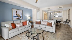 A living room with two sofas, a glass coffee table, and a ceiling fan.