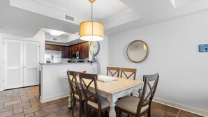 A dining area with a wooden table and chairs, a hanging light fixture, a clock, and a mirror on the wall. - Coastal Hideaway: 3 Bdrm Oceanfront Condo 3rd Flr (North Myrtle Beach)