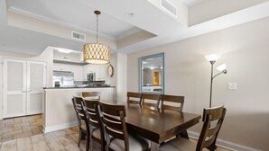 Un comedor con una mesa y sillas de madera, una lámpara colgante y una cocina al fondo.