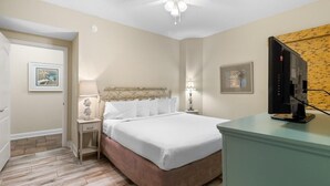 Un dormitorio con una cama, mesitas de noche, ventilador de techo, televisión y obras de arte en las paredes.