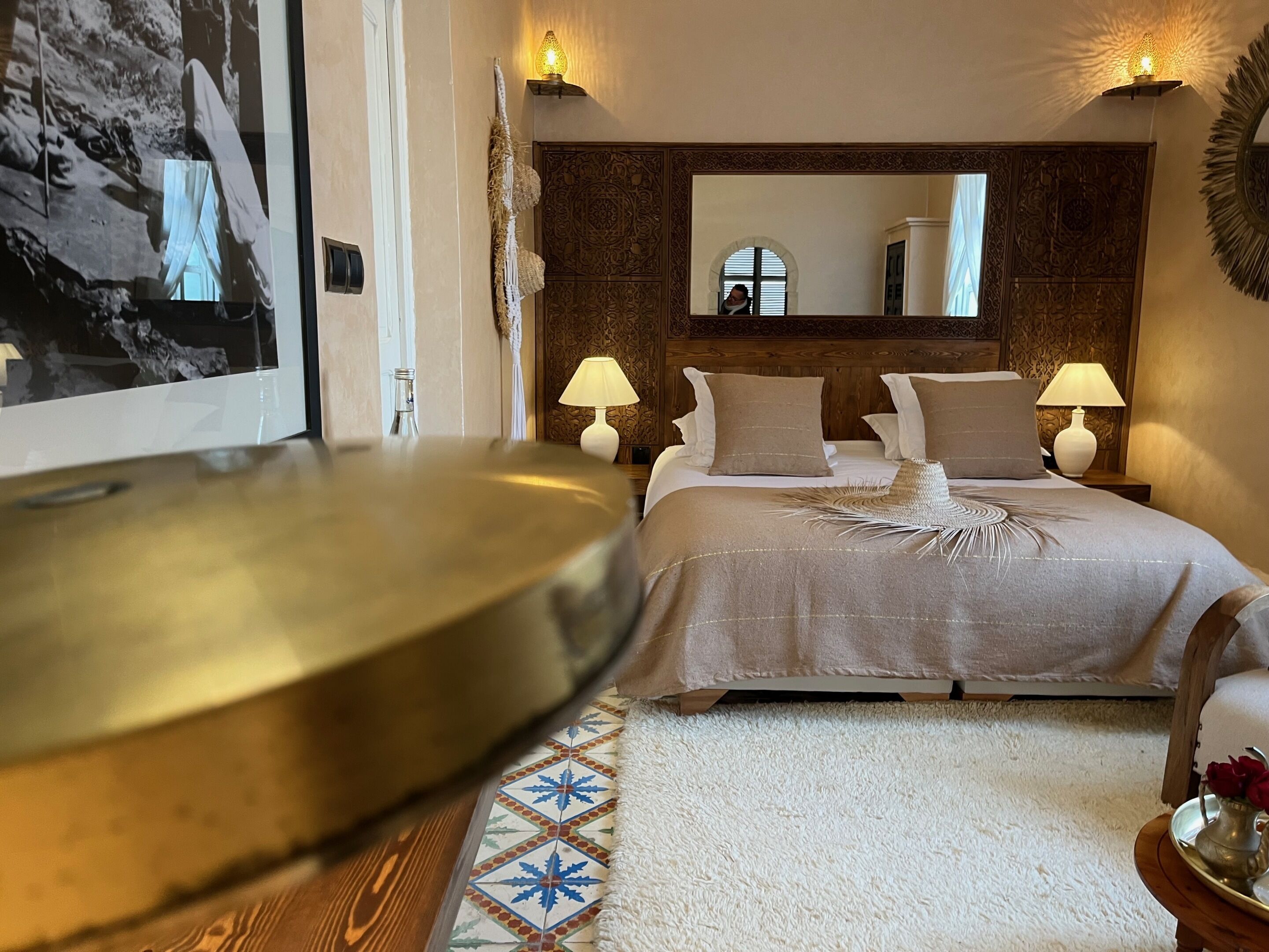A bedroom with a bed, two bedside lamps, a mirror, and a decorative wall panel.