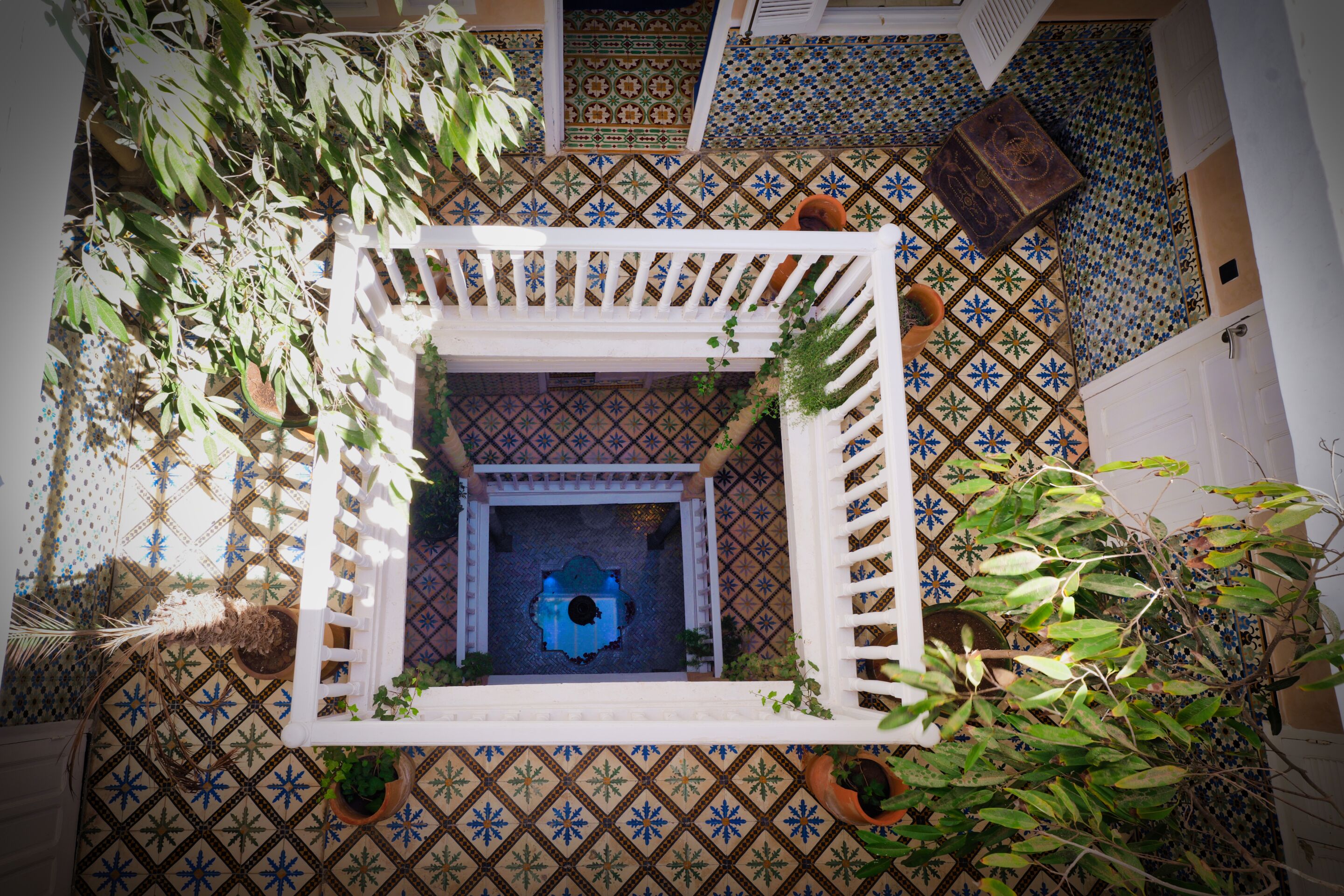 A courtyard with a white lattice structure, patterned tile floor, and potted plants.