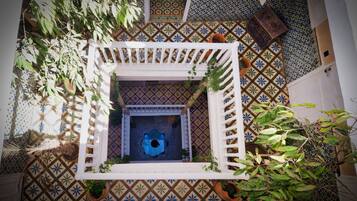 A courtyard with a white lattice structure, patterned tile floor, and potted plants.