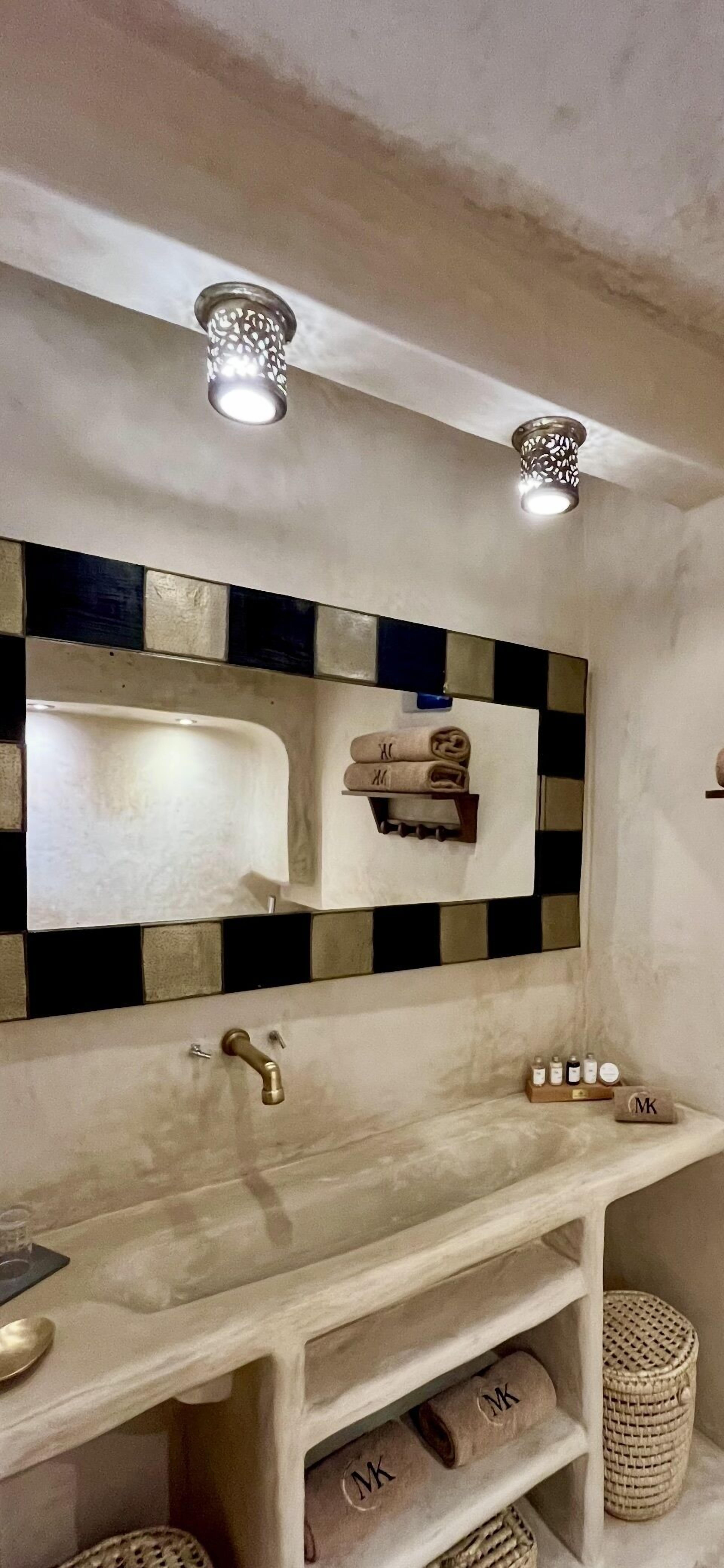Un baño con un lavabo blanco, un espejo con salpicadero a cuadros blanco y negro, y dos luces empotradas.
