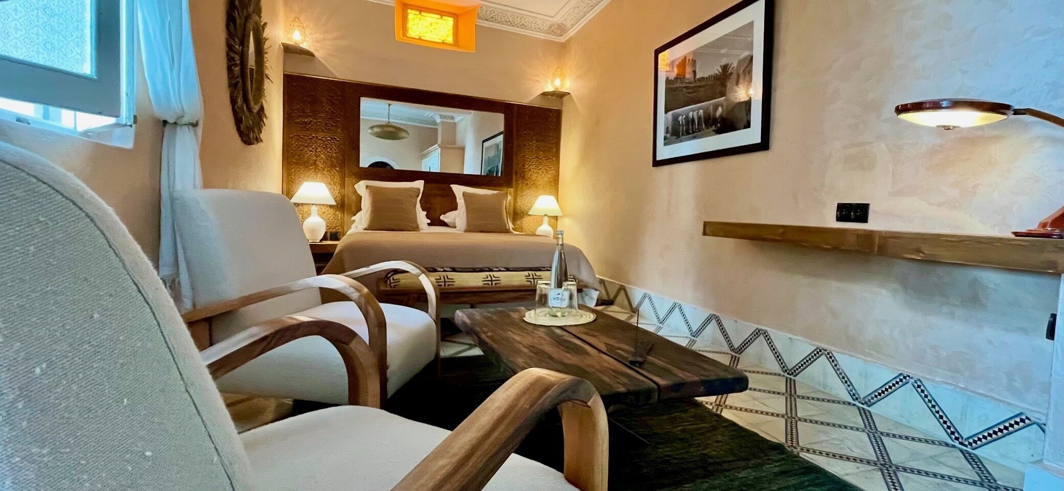 A cozy hotel room with a bed, two chairs, a small table, and a mirror.