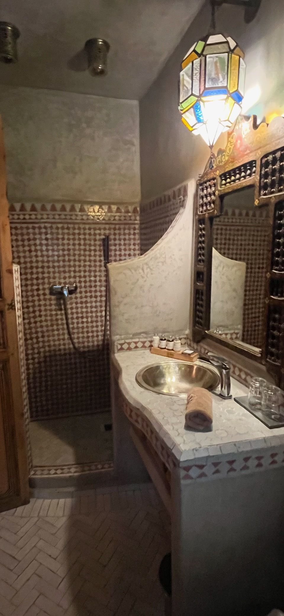 A bathroom with a patterned tile wall, a sink with a mirror, and a shower area.