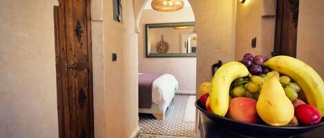 A hallway with a fruit bowl on a counter, a bed with a white blanket, and a patterned floor.