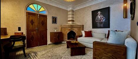 Un salón acogedor con chimenea, un sofá, una mesa de centro de madera y una alfombra estampada.