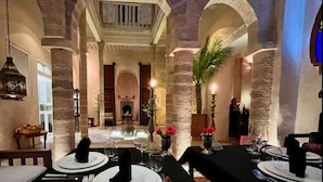 A dining area with stone columns, tables set for a meal, and a fireplace in the background. - RIAD MALAÏKA (Essaouira)