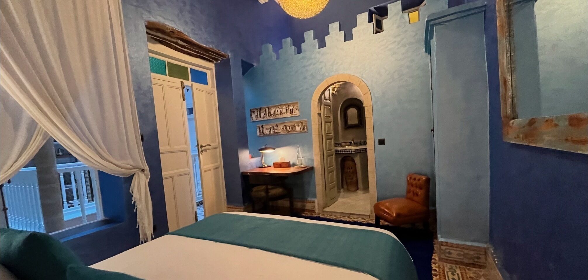 A bedroom with a bed, a desk, a chair, and a decorative archway.