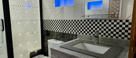 A bathroom with a checkered tile backsplash, a sink with a mirror above it, and a toilet with a glass door.
