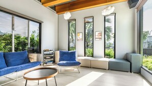 A modern living room with a sofa, armchair, and coffee table. Large windows provide natural light and views of greenery outside. - Ning Xia Time Villa (Dongshan)