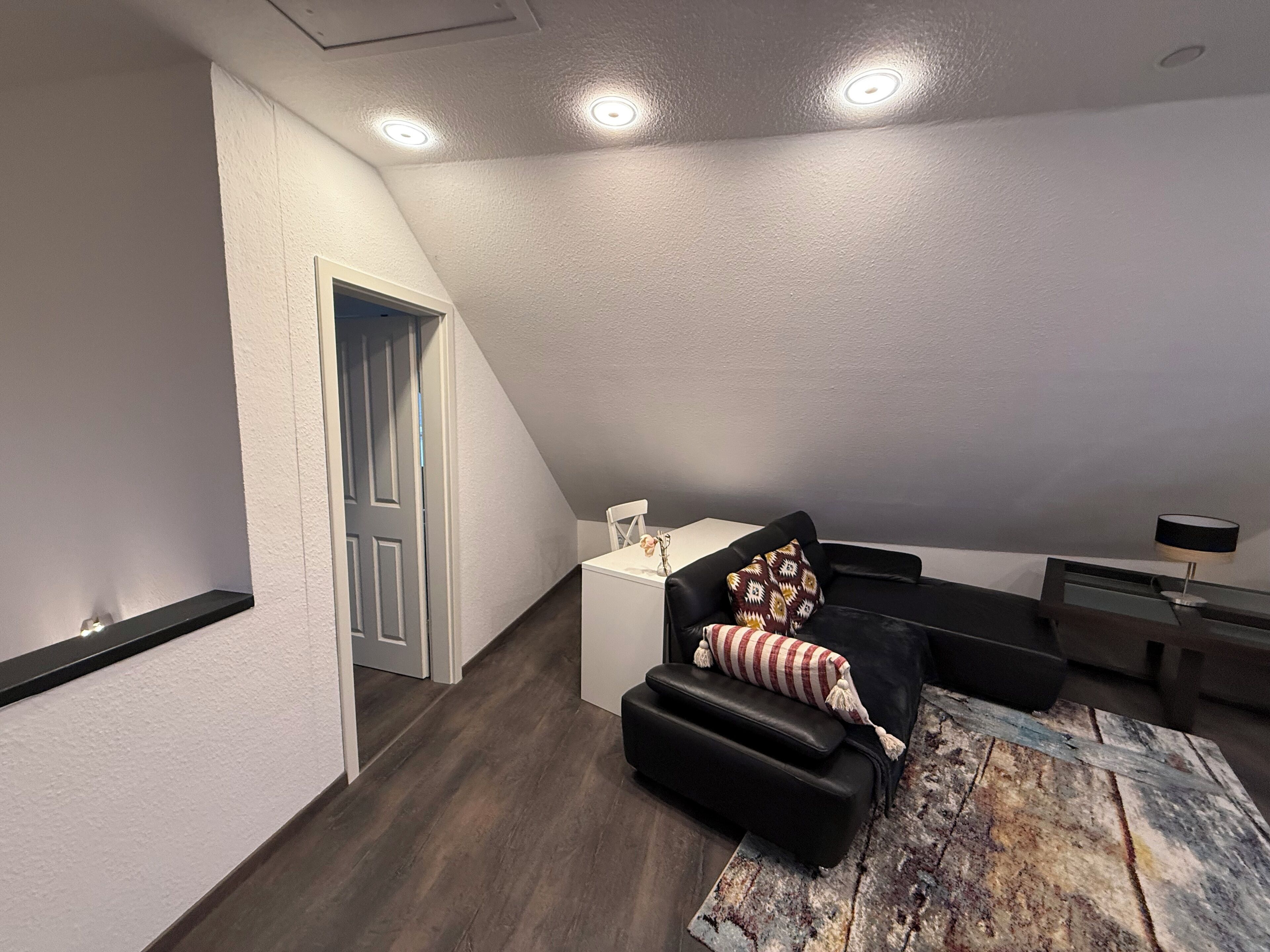 A modern loft bedroom with a sloped ceiling, built-in seating, and a large window.