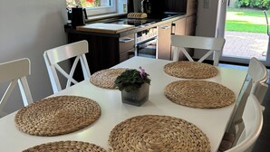A modern kitchen with a dining table set with woven placemats and white chairs. - Modern House Gehrden contactless garden (Gehrden)