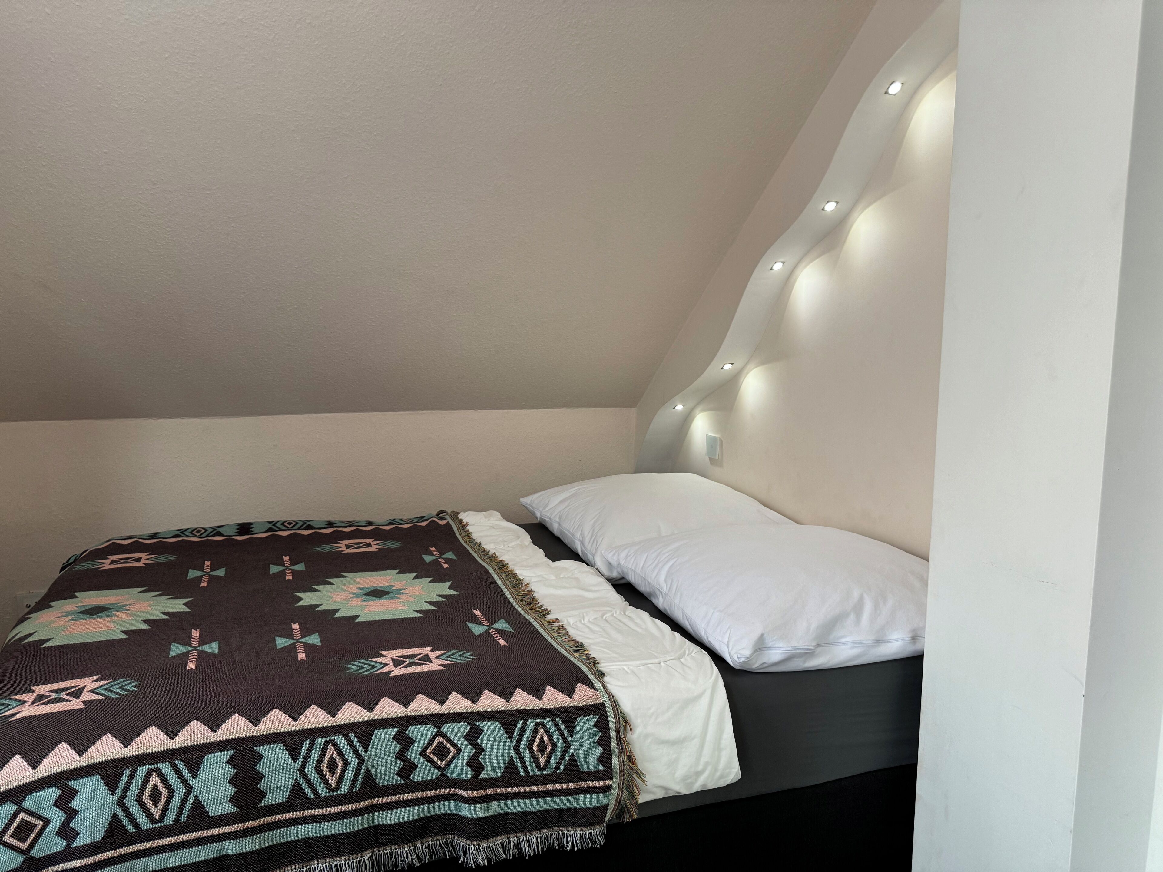 Une chambre à coucher avec un lit, une couverture à motifs et une tête de lit dotée d’un éclairage intégré.