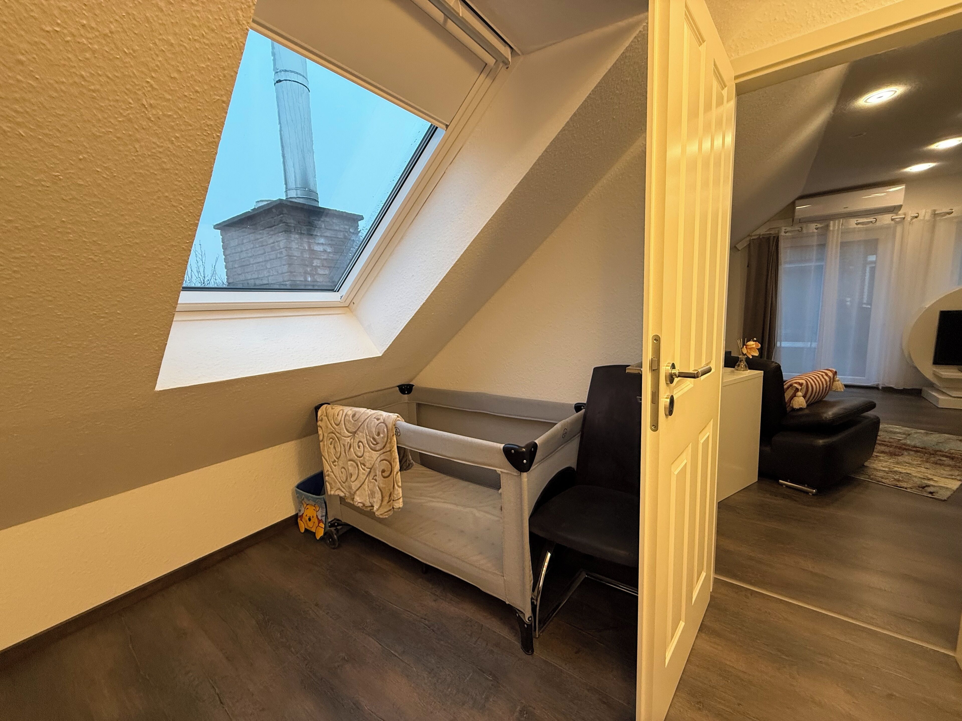Un dormitorio tipo loft con tragaluz, cama, sillón y televisor en la sala.