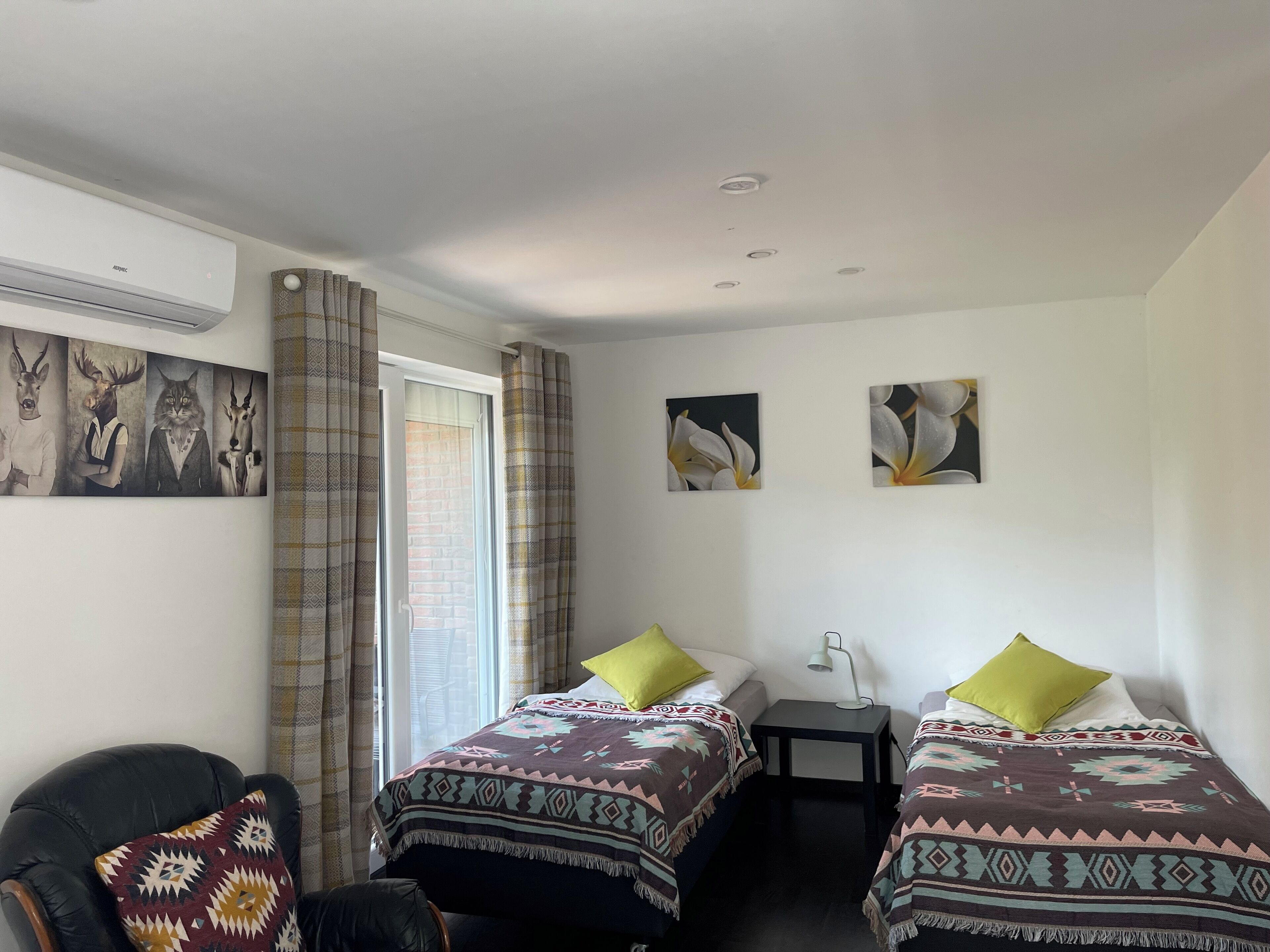 Ein Zimmer mit zwei Betten, einem Sessel, einem Schreibtisch und einem Fenster mit Vorhängen.