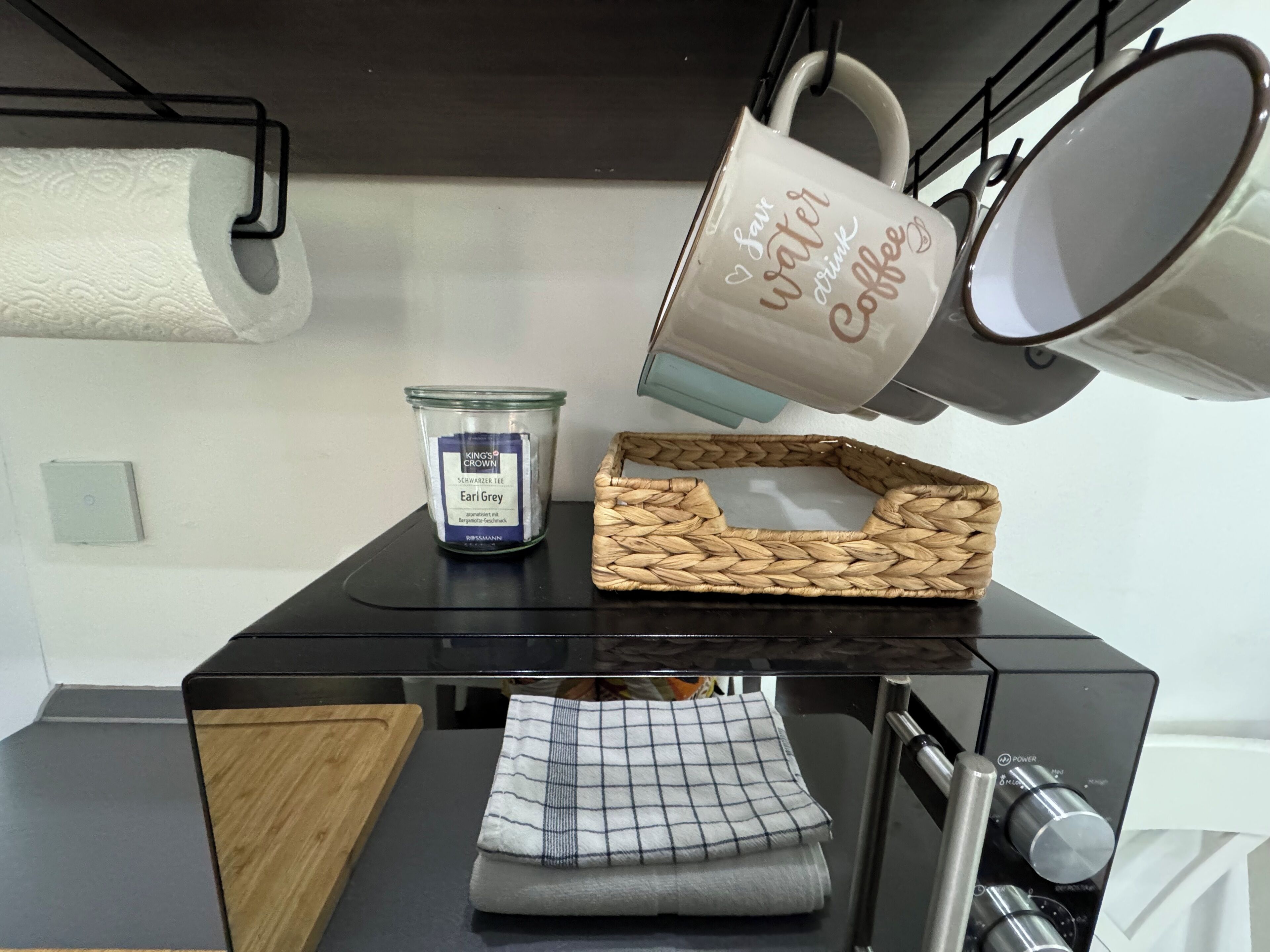 Una encimera de cocina con una cafetera, un tarro de té, una cesta tejida y un mantel a cuadros.