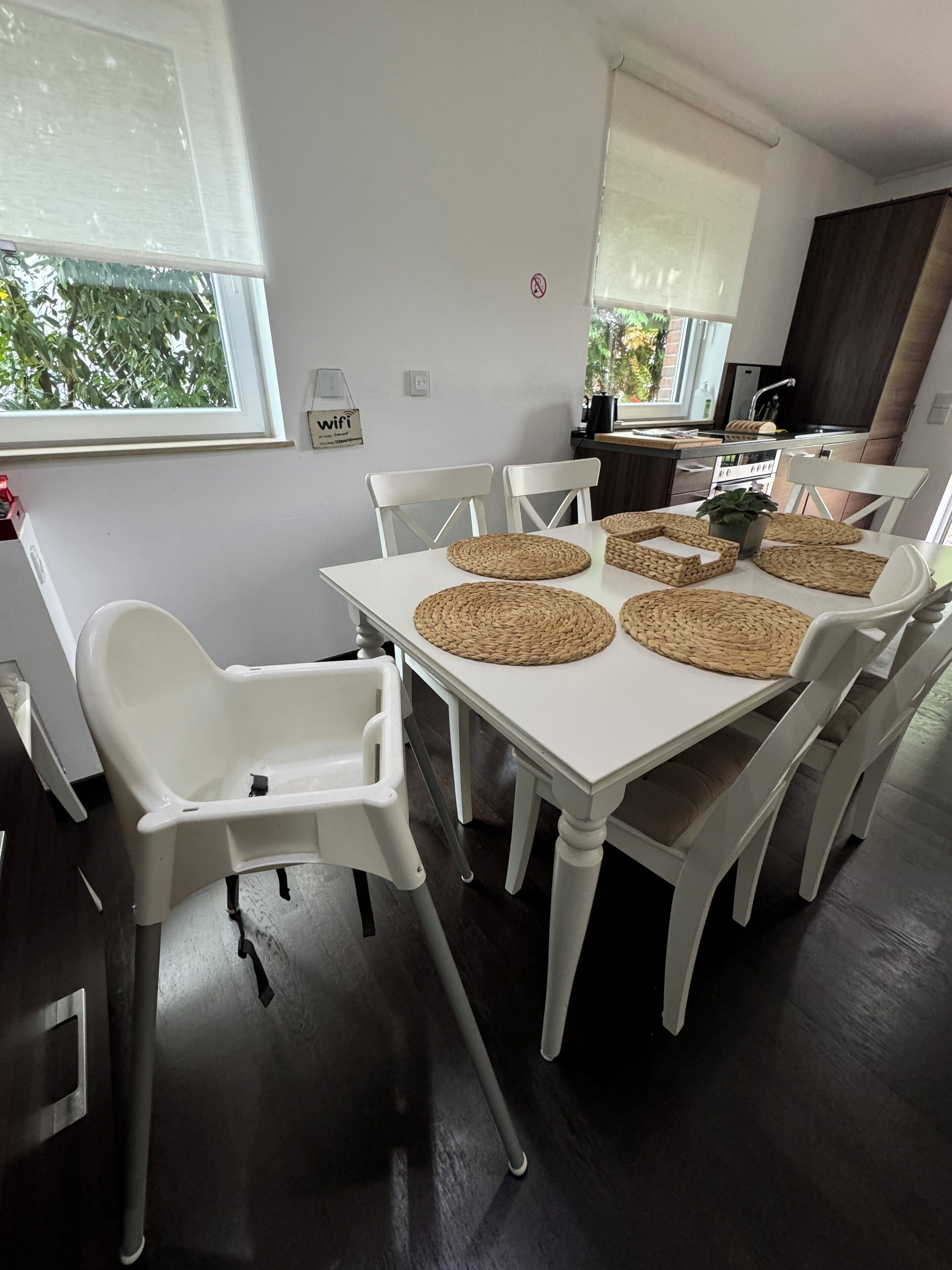 A dining area with a white table, woven placemats, and white chairs.