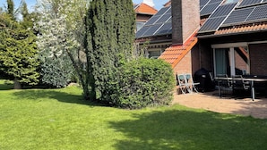 A residential property with a well-maintained lawn, a brick chimney, solar panels on the roof, and a satellite dish. - Modern House Gehrden contactless garden (Gehrden)