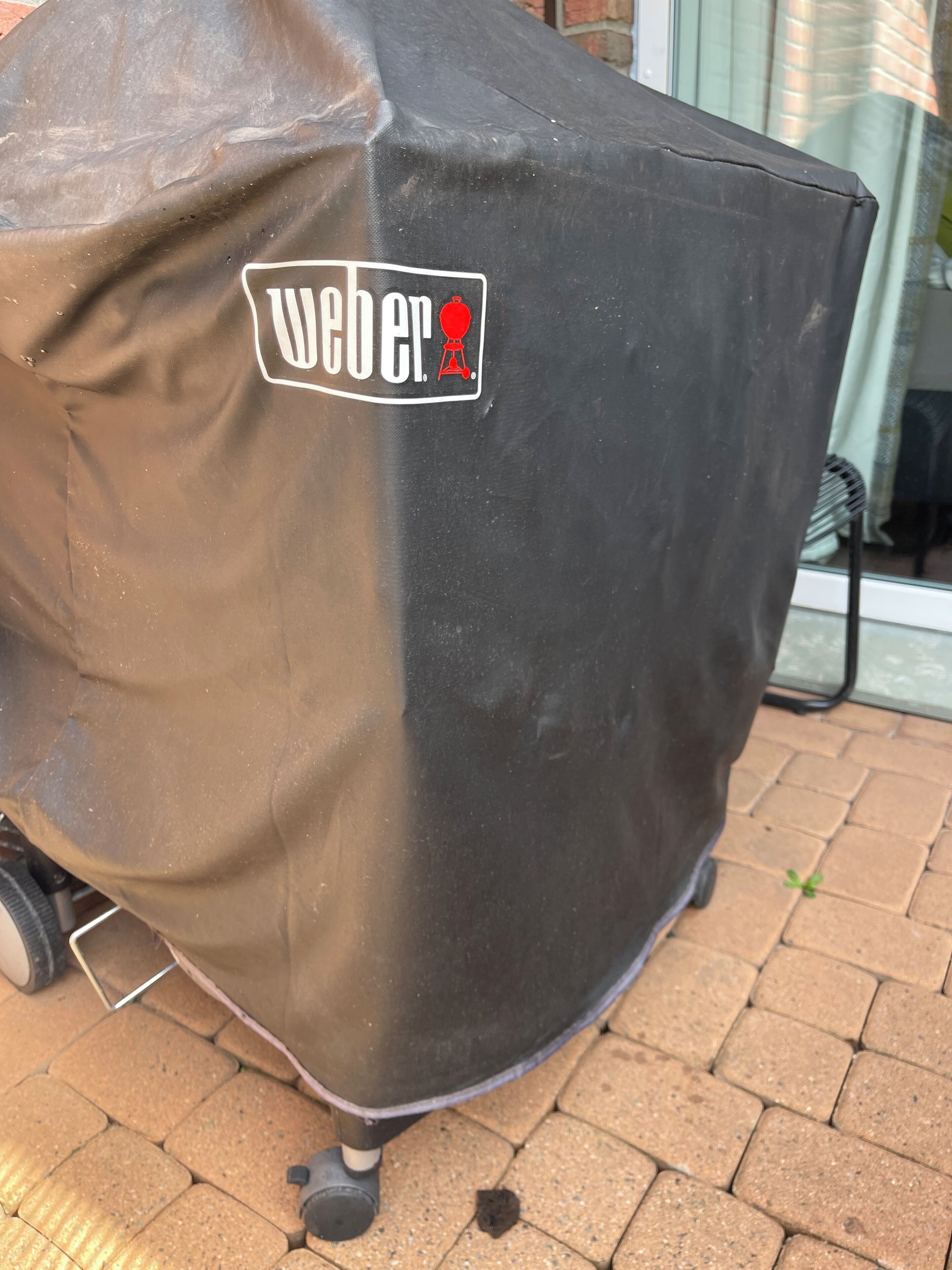 Ein überdachter Grill mit Logo und einem roten Gegenstand, auf einer Pflasterterrasse platziert.