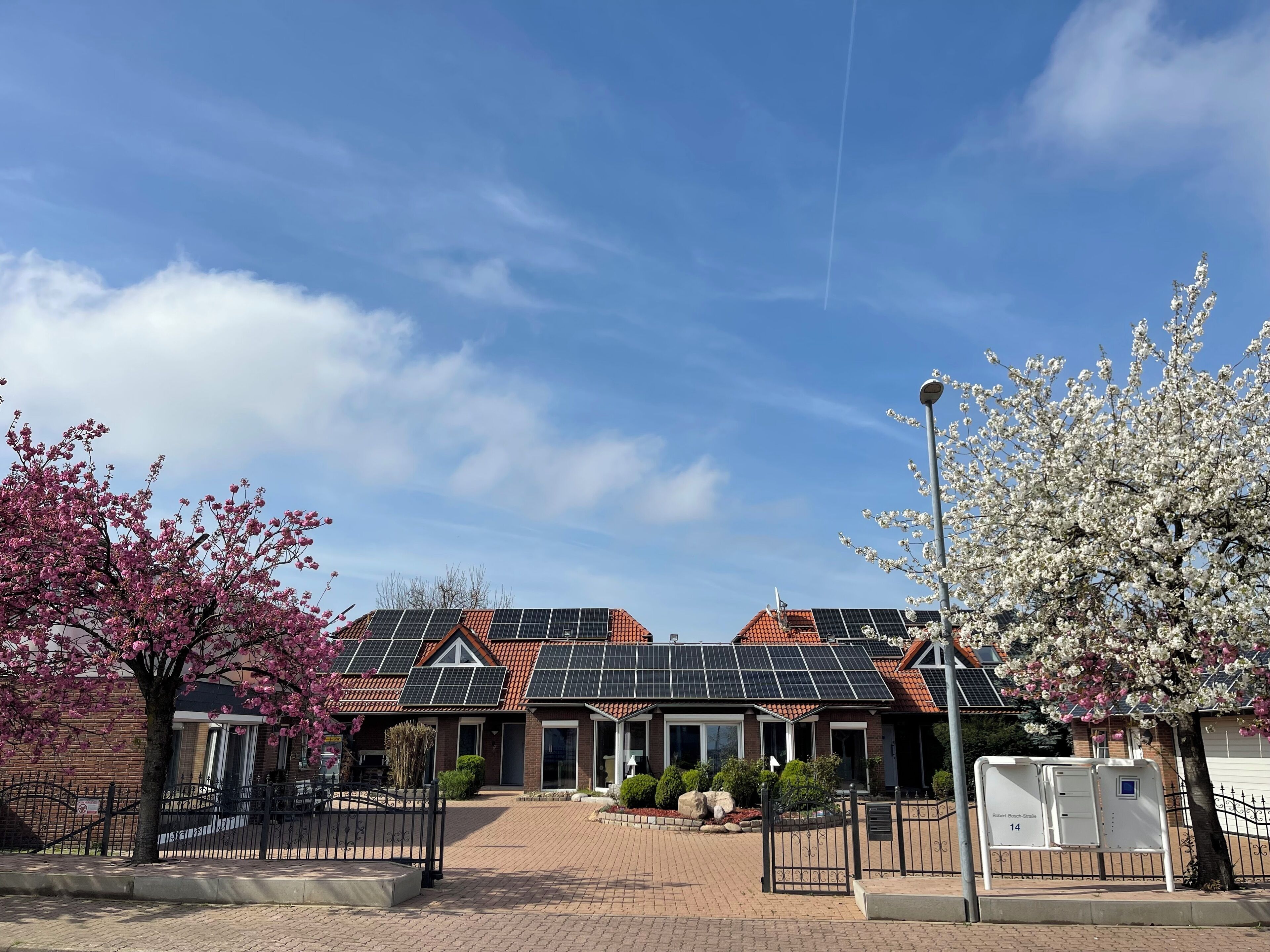 A residential building with a brick facade, solar panels on the roof, and a paved driveway.