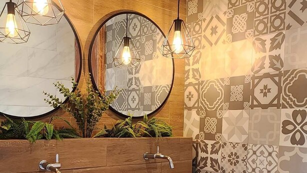 A modern bathroom with wooden vanity, two round mirrors, and patterned tiles. - HOP TERRACOTA Summary (Ica)