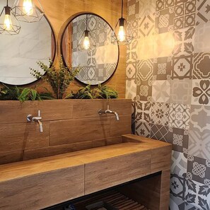 A modern bathroom with wooden vanity, two round mirrors, and patterned tiles.