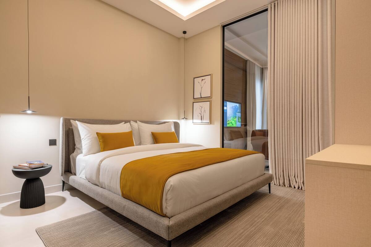 Moderni hotellihuone, jossa on suuri sänky, yöpöytä, pieni sivupöytä ja suuri ikkuna, jossa on verhot.