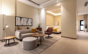 Un salon moderne comprenant un canapé, un pouf et un fauteuil, une table basse et un tableau accroché au mur.