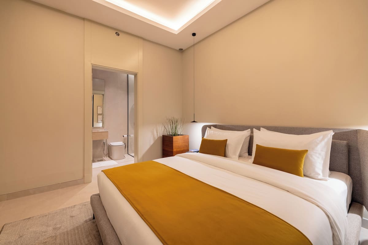 Moderni hotellihuone, jossa on suuri sänky, yöpöytä, yövalaisin ja ruukussa oleva kasvi.