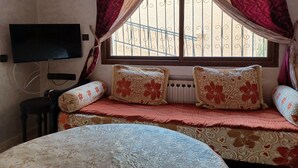 A bedroom with a bed, a TV, a window with curtains, and a radiator.