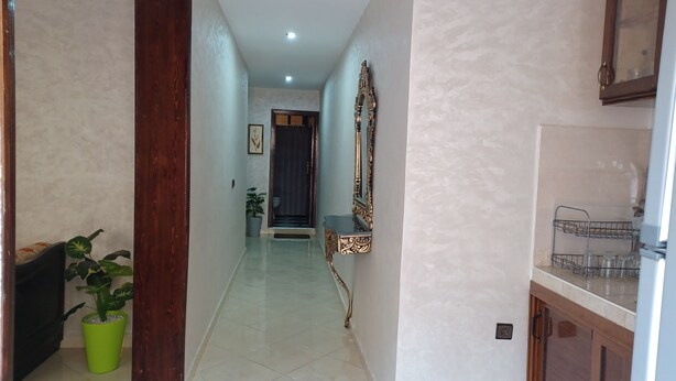 A hallway with a wooden door, a green potted plant, a mirror, and a cabinet with a metal rack.