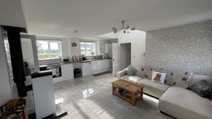 A spacious living room with a sofa, coffee table, and a view of the kitchen. - Barn Retreat/ Hottub/ Bbq/ Petsok/wi-fi (Evesham)