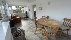 A dining area with a round wooden table and chairs, a sofa, a wicker basket, and a view of the outdoors through a large window. - Barn Retreat/ Hottub/ Bbq/ Petsok/wi-fi (Evesham)