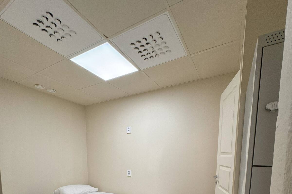 Une petite chambre propre, avec deux lits simples, une armoire et un plafond doté d’une ventilation.