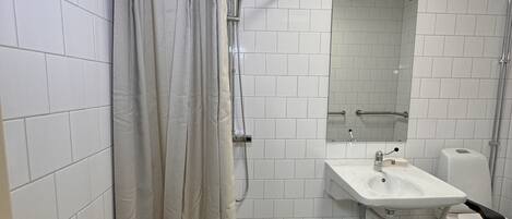 Un baño con paredes de azulejos blancos, una ducha con cortina, un lavabo y un inodoro.