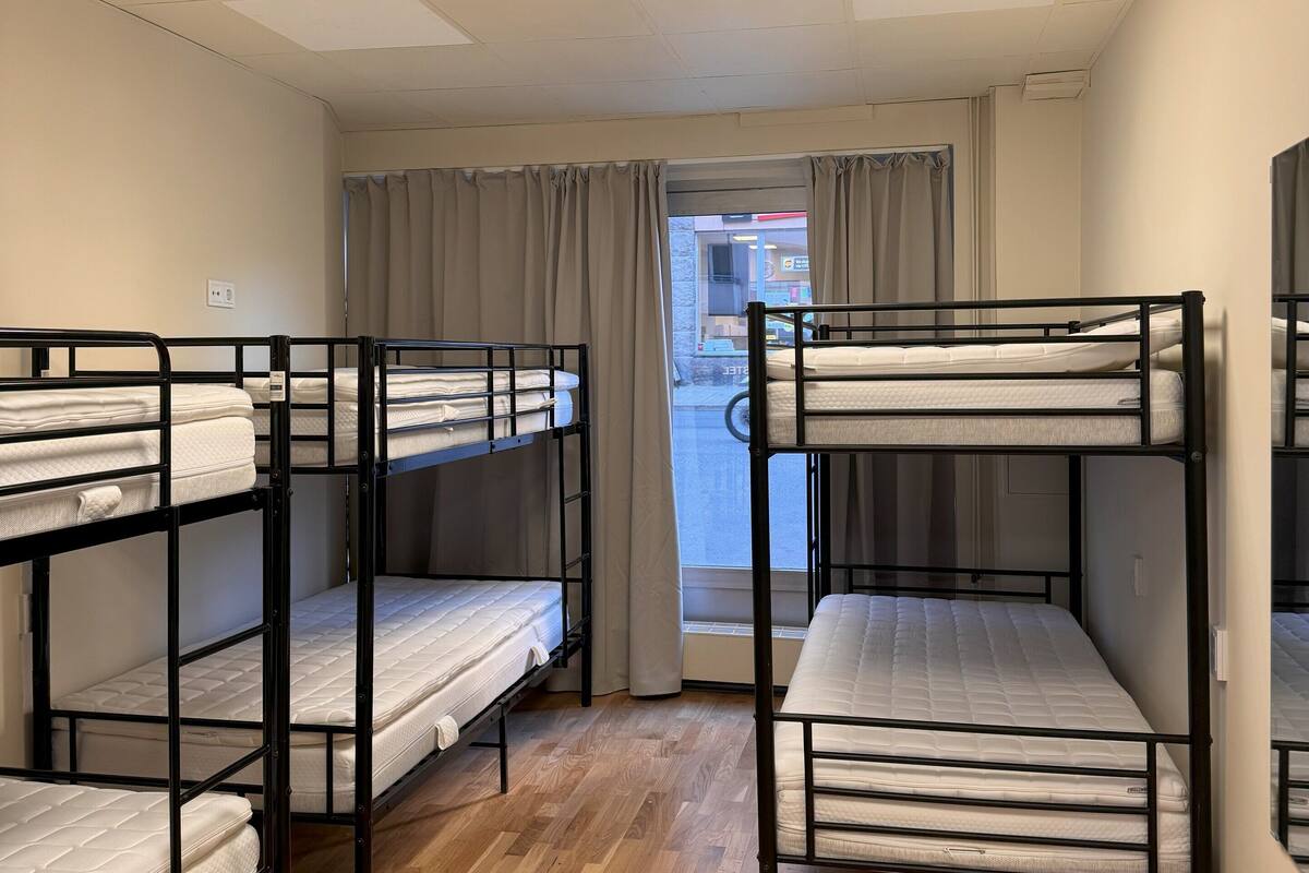 Une chambre avec des lits superposés, un plancher en bois, une fenêtre avec des rideaux et un plafond doté d’un éclairage encastré.